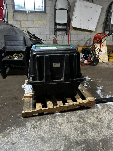 Large black plastic crate on wooden pallet in workshop