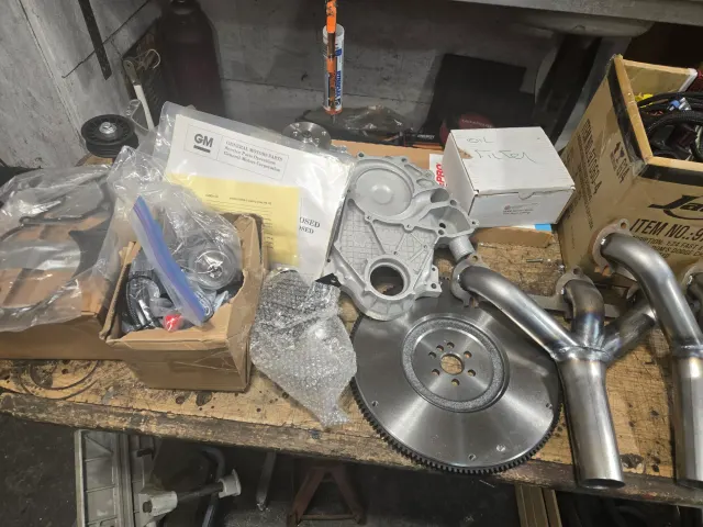 New engine parts on bench: timing cover, flywheel, headers