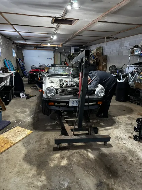 Engine hoist positioned over classic roadster in garage