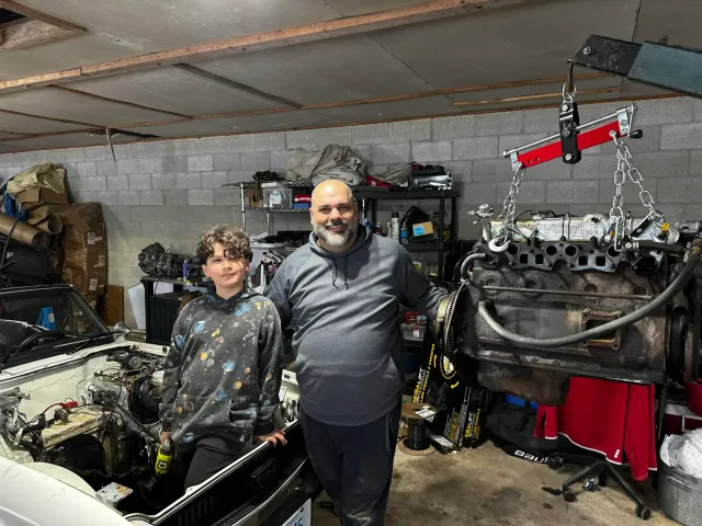 Father and son beside engine on hoist in garage