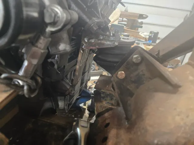Cluttered close-up of steering column and rusty bracket